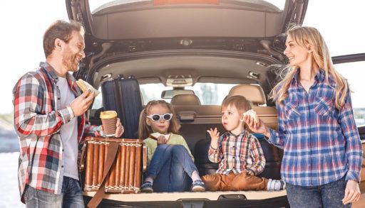 Family of four on a road-trip eating lunch together at the rear of their SUV