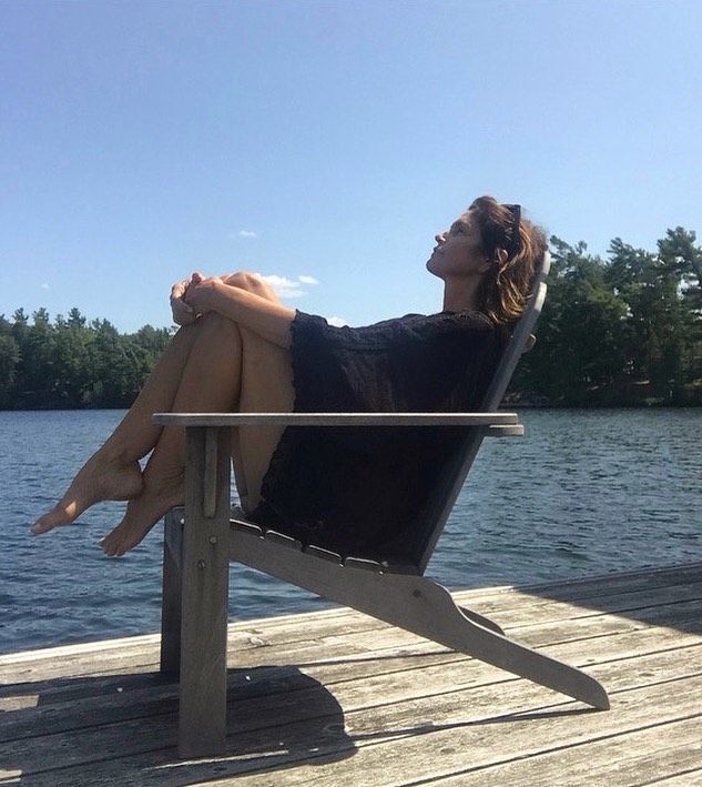 Cindy Crawford sitting in a Muskoka chair on the dock
