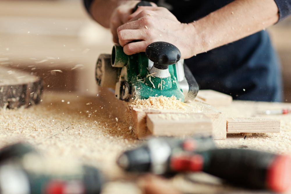 Closeup crop hands of young woodworker making wooden detail and using electric sanding machine at workplace covered with dust near equipment