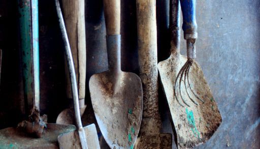 old dirty farm metal garden tools as shovels and rakes hanging on the wall on nails
