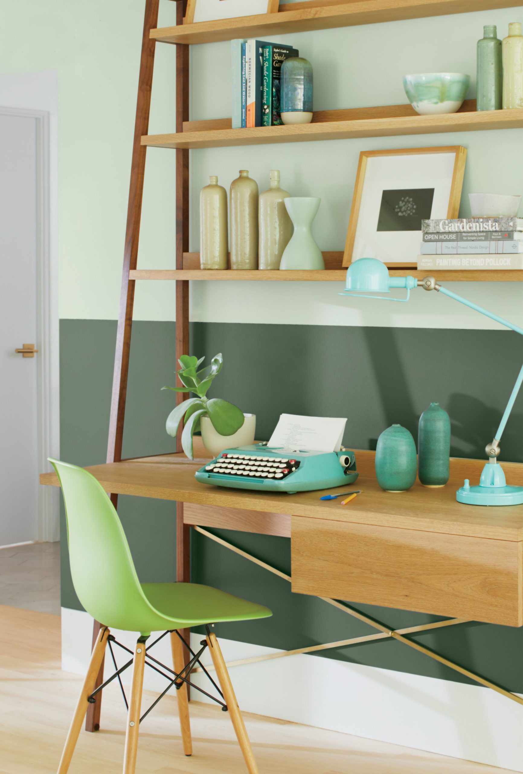 A desk with shelves sits in front of a two-toned green wall