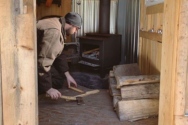 man chopping firewood for a woodstove in a cabin