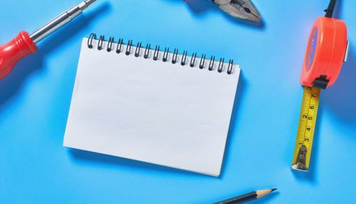 Different tools lies near blank paper notebook on blue desk in workshop, chores