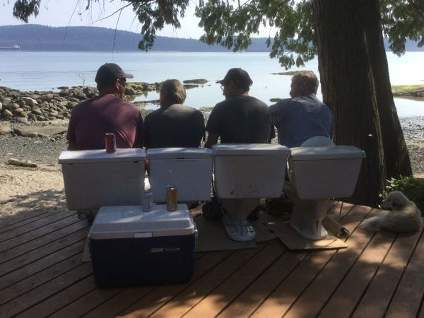 four men sitting on toilets
