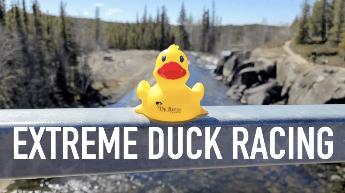 Yellow rubber duck sitting on railing over river with text "Extreme Duck Racing" under it.
