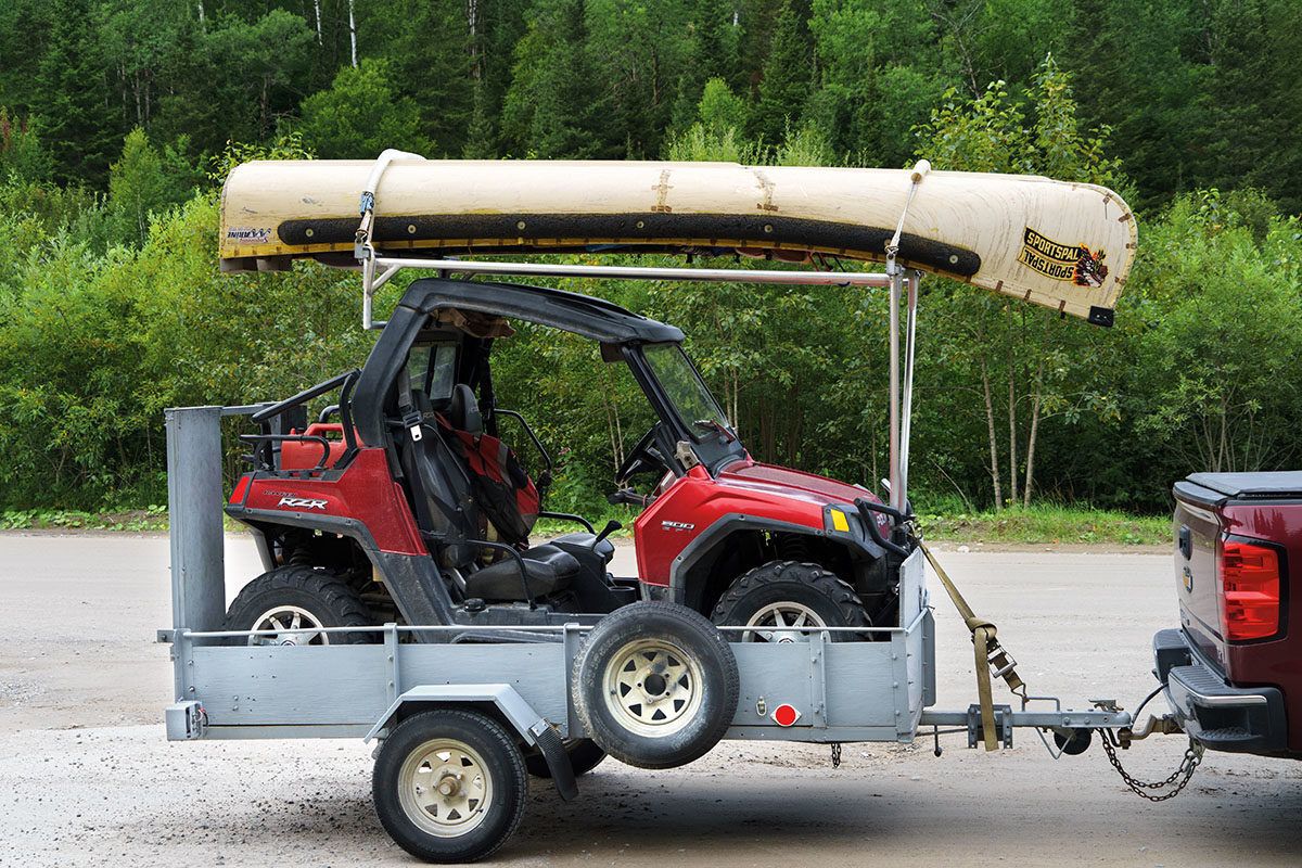 small utility vehicle on a small utility trailer with a canoe on top attached to a truck