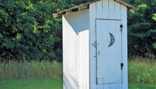A white outhouse in a field