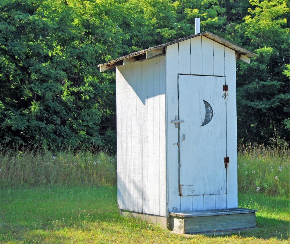 A white outhouse in a field