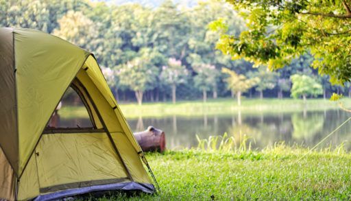 A yellow camping tent beside a lake, surrounded by trees