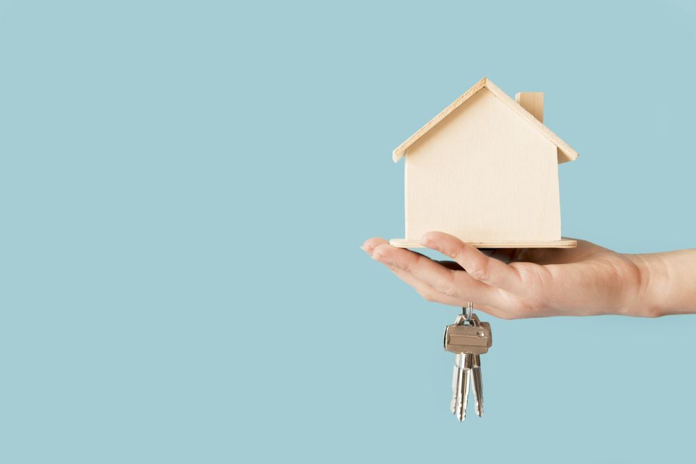 Close-up of young hand holding keys and wooden house model against blue background
