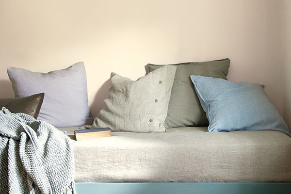 off-white paint colour behind a blue bench with several lightly coloured pillows on it