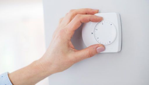 Close Up Of Female Hand On Central Heating Thermostat