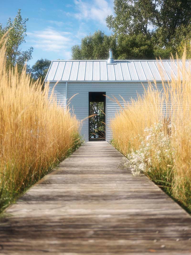 white minimalist cottage at the end of a boardwalk framed by tall grasses