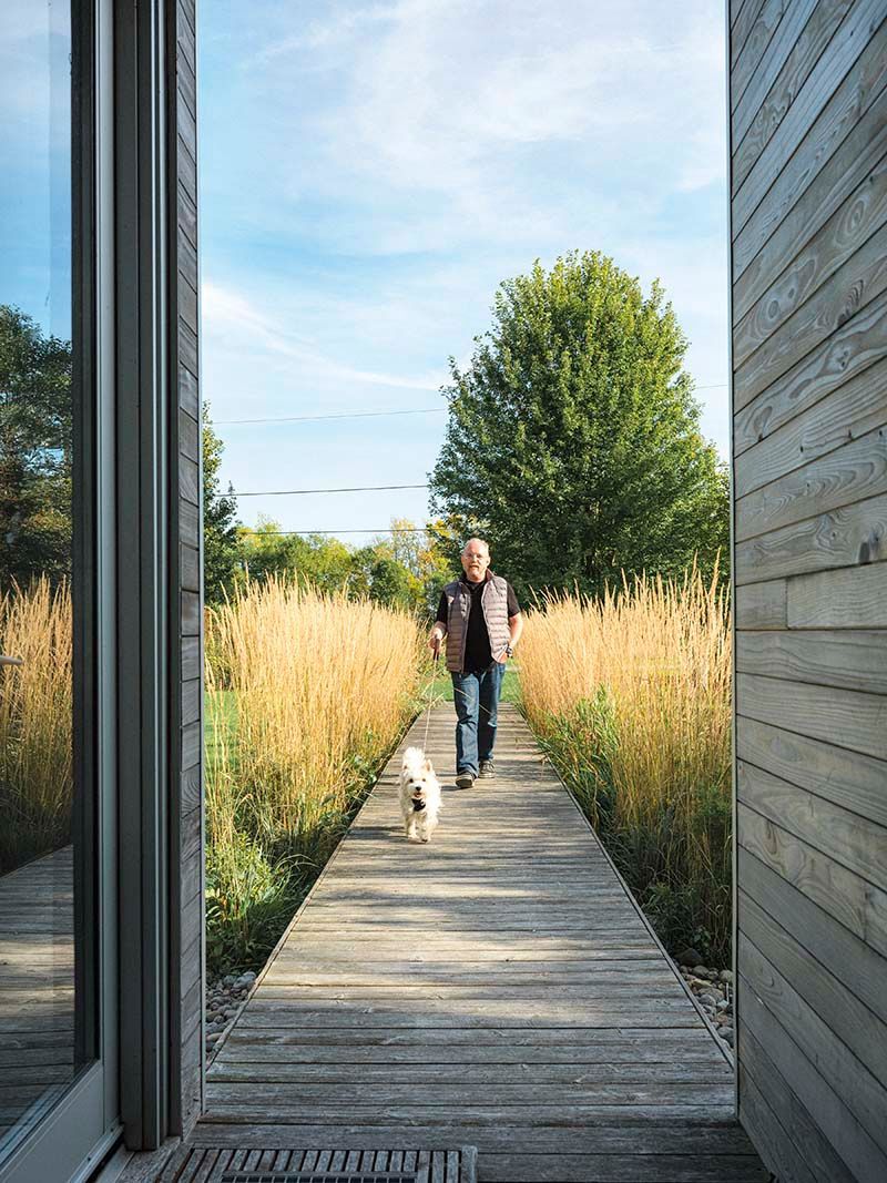 Man walking a white dog walking along a boardwalk towards the cottage
