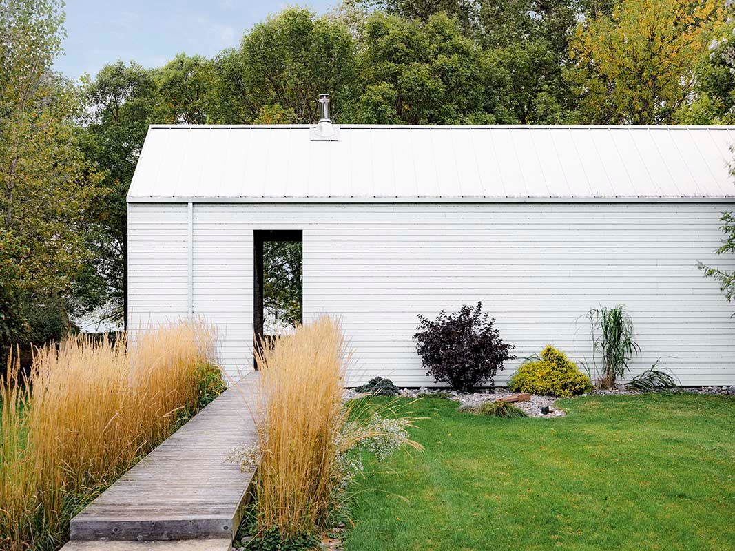 exterior shot of white barnboard cottage with tall grasses framing a boardwalk