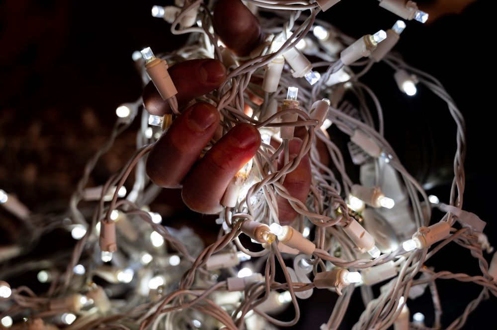 hands gripping tangled Christmas light cords trying to unravel them dangerous wires