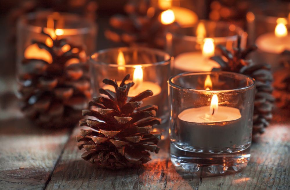 Christmas candles in glass jars with decorative pinecones on wooden table surface