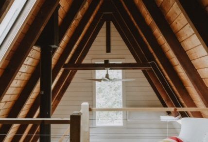upper level of the aframe with exposed beams and a white chair in the corner