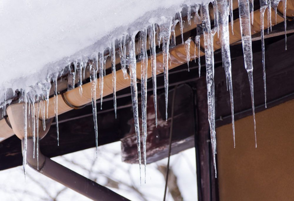 Sharp icicles and melted snow hanging from eaves of roof. Beautiful transparent icicles slowly gliding of a roof