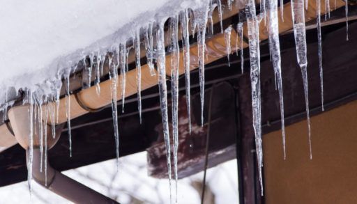 Sharp icicles and melted snow hanging from eaves of roof. Beautiful transparent icicles slowly gliding of a roof