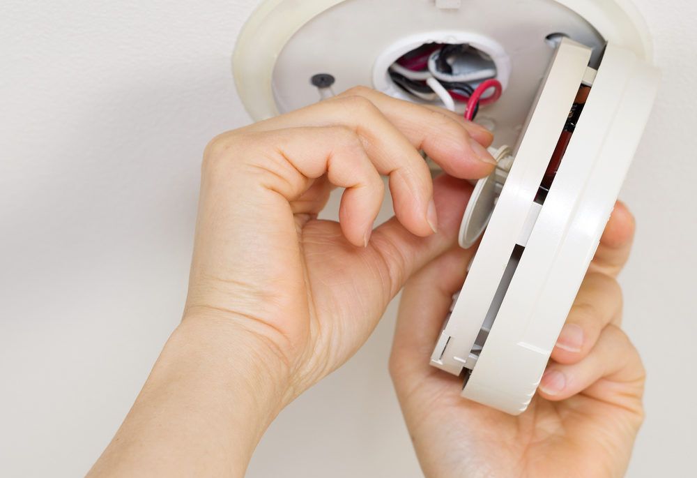 Horizontal photo of female hands taking home smoke detector apart with white ceiling background