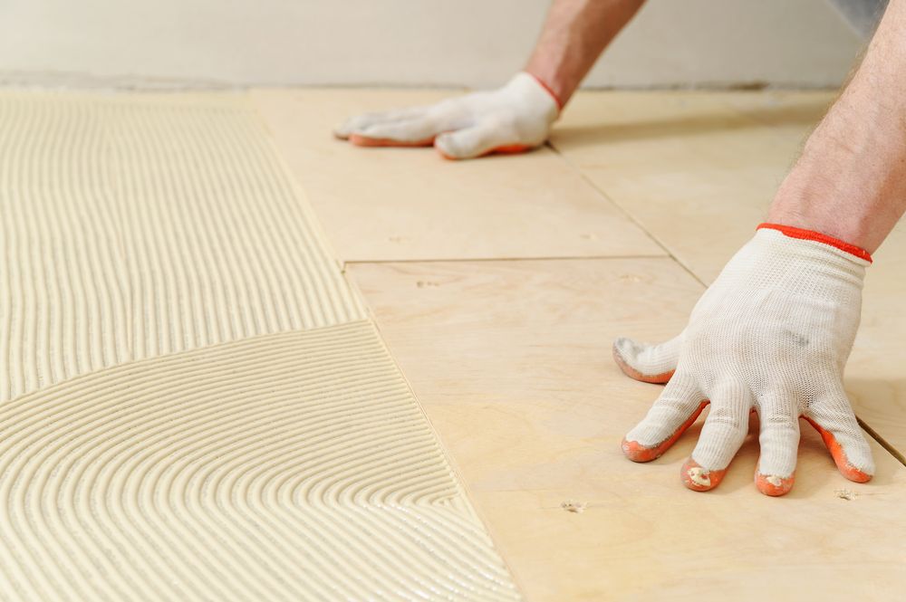 A close-up of gloved hands laying plywood on top of subflooring