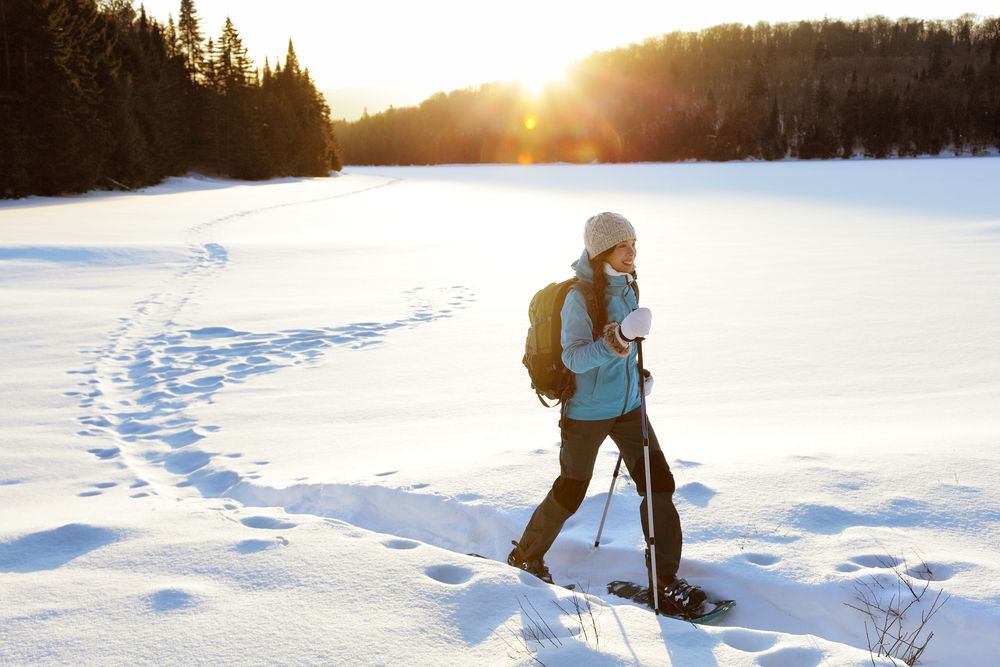 Winter sport activity. Woman hiker hiking with backpack and snowshoes snowshoeing on snow trail forest in Quebec, Canada at sunset. Beautiful landscape with coniferous trees and white snow.