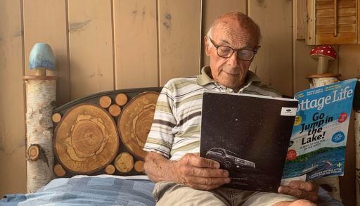 Jim Curtis laying on a bed and reading a Cottage Life magazine in front of his mushroom and birch headboard project