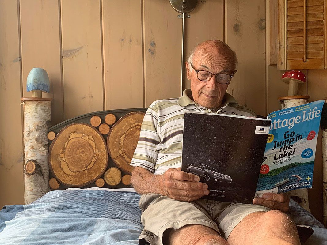 Jim Curtis laying on a bed and reading a Cottage Life magazine in front of his mushroom and birch headboard project