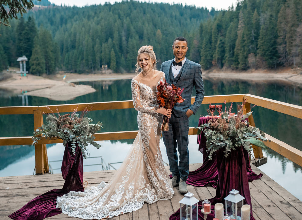 A bride and groom standing on a deck overlooking a lake
