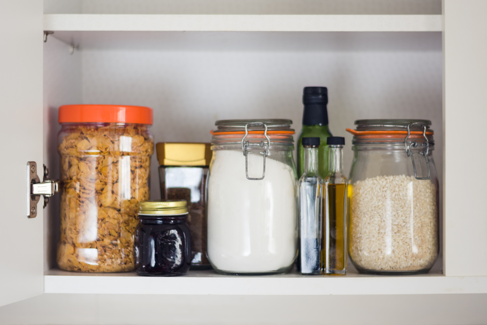 stocked kitchen cupboard with food - jars and containers of cereals, jam, coffee, sugar, flour, oil, vinegar, rice
