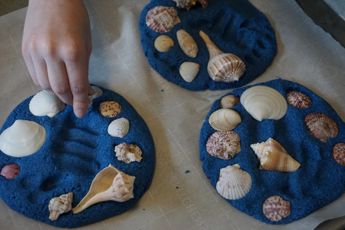 blue coloured sand imprinted with handprints and seashells