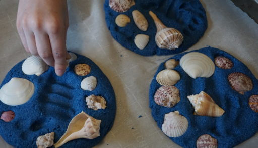 blue coloured sand imprinted with handprints and seashells