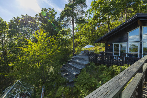 View of facade of typical wooden swedish house with wooden patio. Black walls and white windows with barbecue grill and sitting area with umbrellas and sun beds. 07.25.2020. Geta, Aby, Sweden, building materials