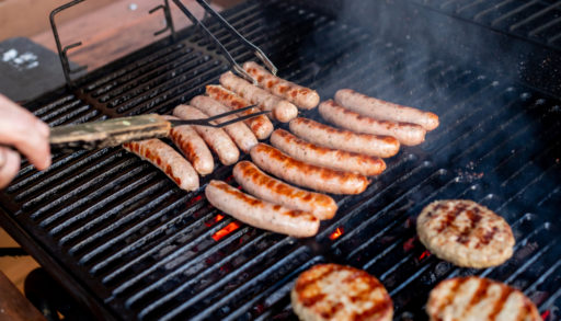 Man at a barbecue grill with smoke.Grilling sausages on barbecue grill. BBQ party.Delicious german sausages or bratwurst