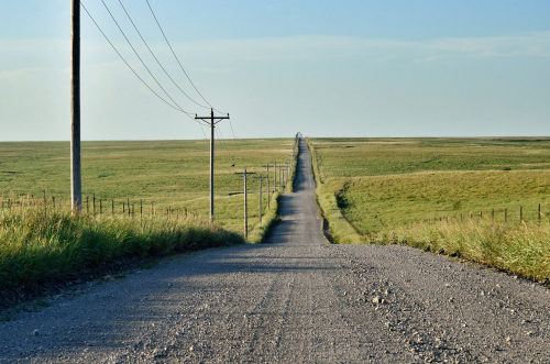 Rural gravel road lined with telephone poles going into distant open prairie, deal-breakers