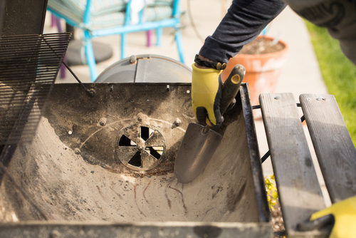 Unknown man cleaning out ashes from charcoal grill, barbecue tune-ups