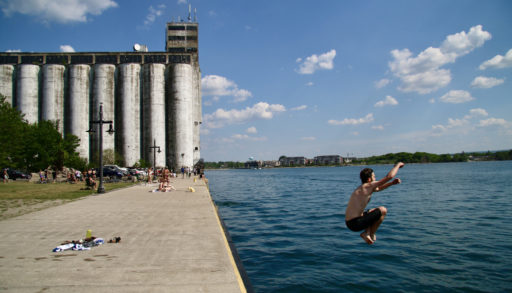 A man jumping into the water with the Collingwood Grain Terminals in the background.