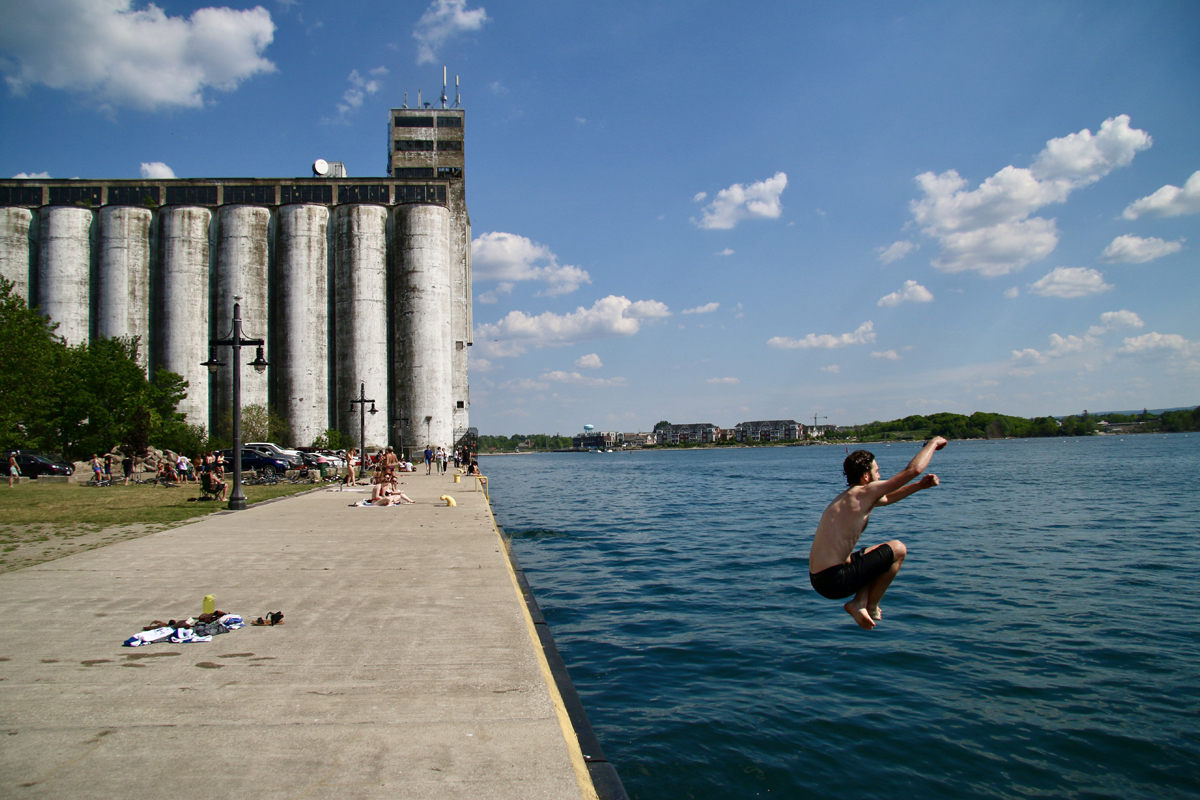 A man jumping into the water with the Collingwood Grain Terminals in the background.
