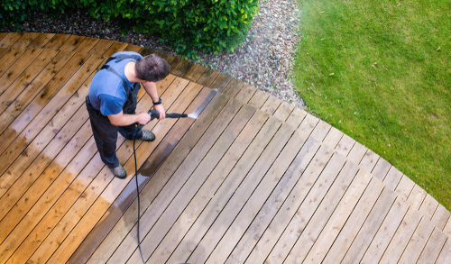man cleaning terrace with a power washer - high water pressure cleaner on wooden terrace surface, pressure washer