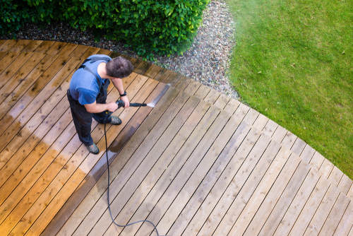 man cleaning terrace with a power washer - high water pressure cleaner on wooden terrace surface, pressure washer