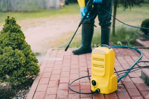 Man cleaning red, conrete pavement block using high pressure water deck. Paving cleaning concept. Man wearing waders, protective, waterproof trousers and gloves doing spring jobs in the garden. pressure washer