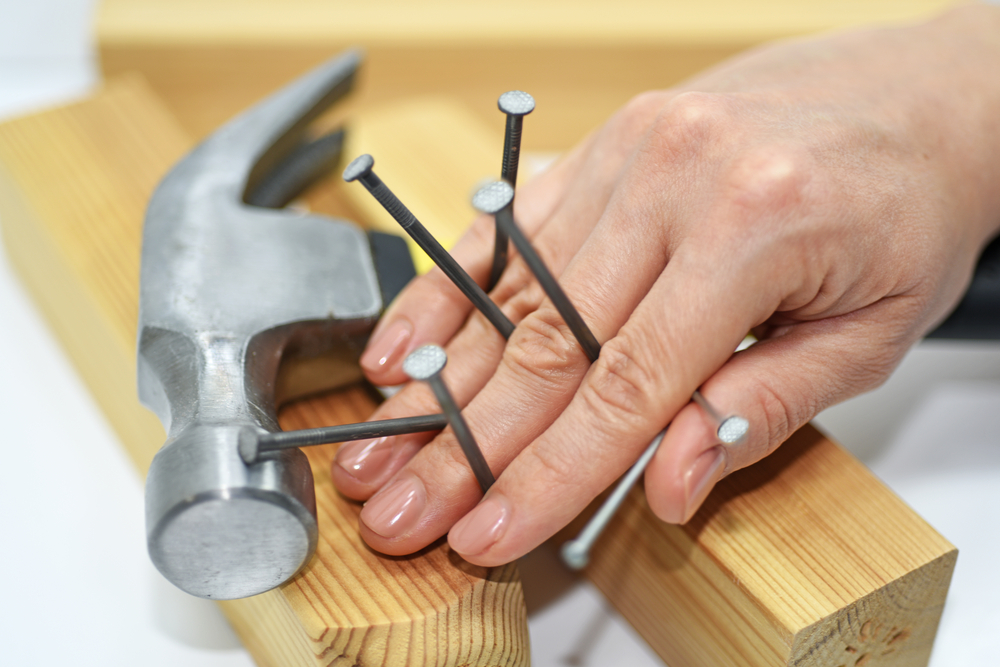 A close-up of a hand, a hammer, and several nails