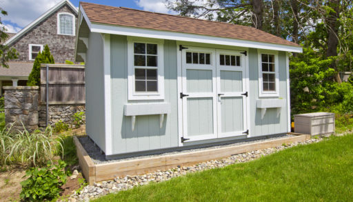 A blue-grey garden shed sitting on gravel