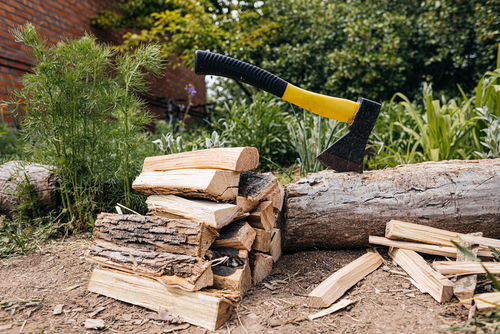A sharp hatchet with a yellow handle splits firewood for a bonfire on a stump in the spring garden. yardwork tools