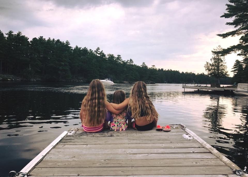 Three kids sitting at the end of a dock