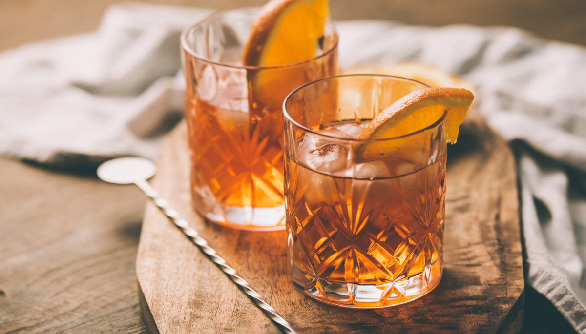 two old fashioned cocktails at cottage in highball glass on wooden plank