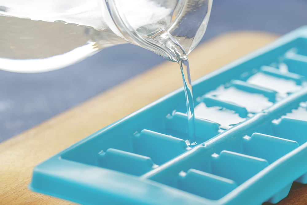 Pouring water into ice cube tray on the kitchen table. Making ice cubes for summer refreshing drinks. measure