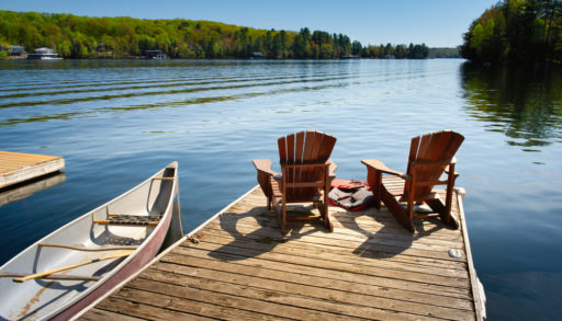A dock with two chairs and a canoe tied up alongside