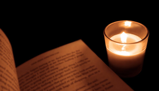 candle in glass holder beside a book